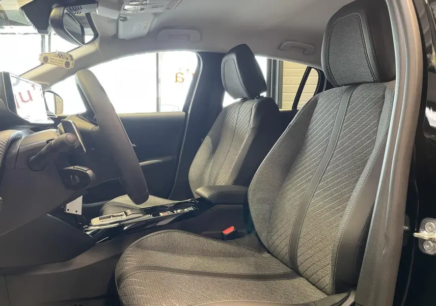 Vue intérieure côté conducteur de la Peugeot 208 noire 2025, sièges tissu gris avec surpiqûres Quartz et volant cuir.