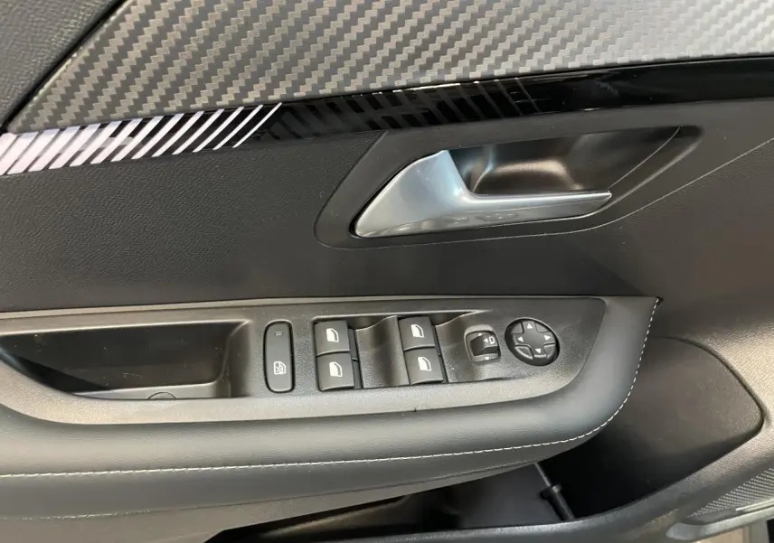 Détail de la porte avant gauche noire de la Peugeot 208 1.2i Hybrid avec commandes des vitres et insert carbone.