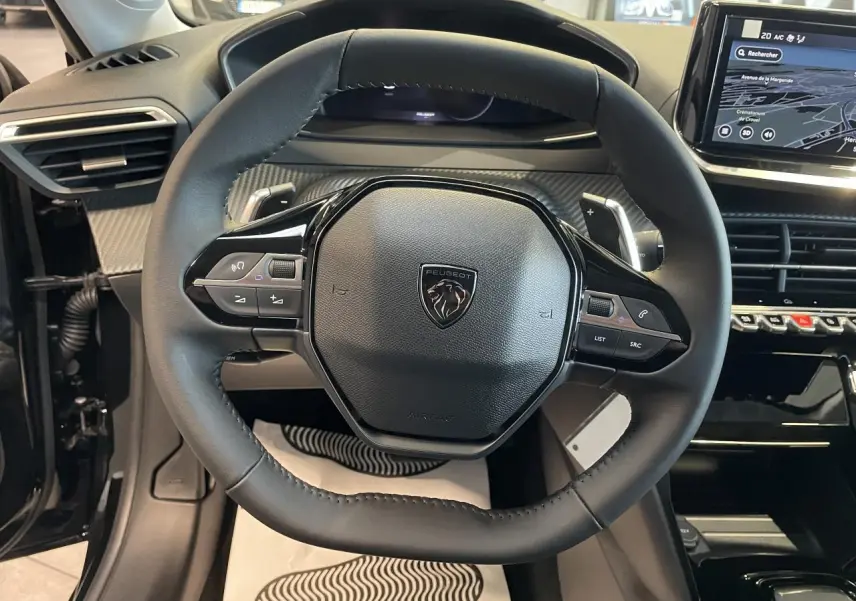 Vue rapprochée du volant cuir noir et du tableau de bord numérique de la Peugeot 208 hybride 2025 Allure.
