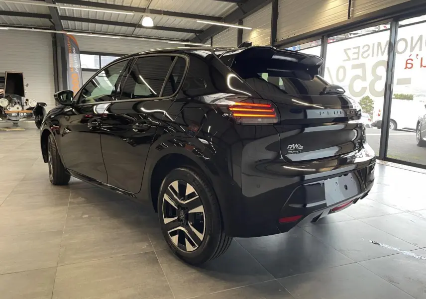 Peugeot 208 noire vue en 3/4 arrière droit dans un showroom, avec feux arrière LED allumés et jantes alliage.