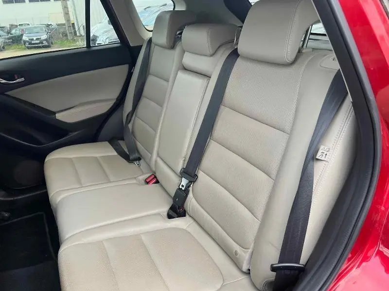 Vue côté gauche de la banquette arrière cuir beige du Mazda CX-5 Soul Red Métallisé avec ceintures de sécurité noires.