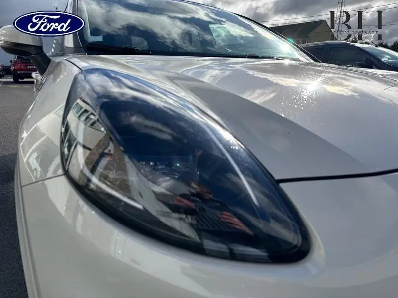 Gros plan sur le phare avant gauche du Ford Puma blanc Premium Metropolis sous un ciel nuageux.