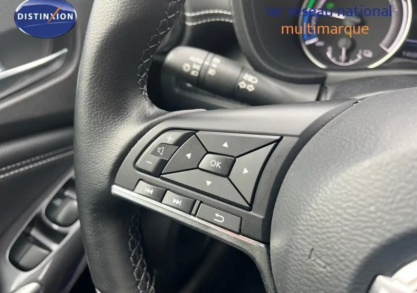 Gros plan sur les commandes multifonctions noires du volant du Nissan Juke blanc nacré 2024, avec tableau de bord en arrière-plan.