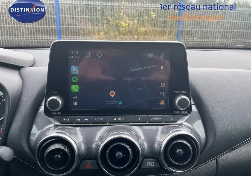 Vue rapprochée de la console centrale du Nissan Juke 2024, écran tactile avec navigation et aérateurs ronds chromés.