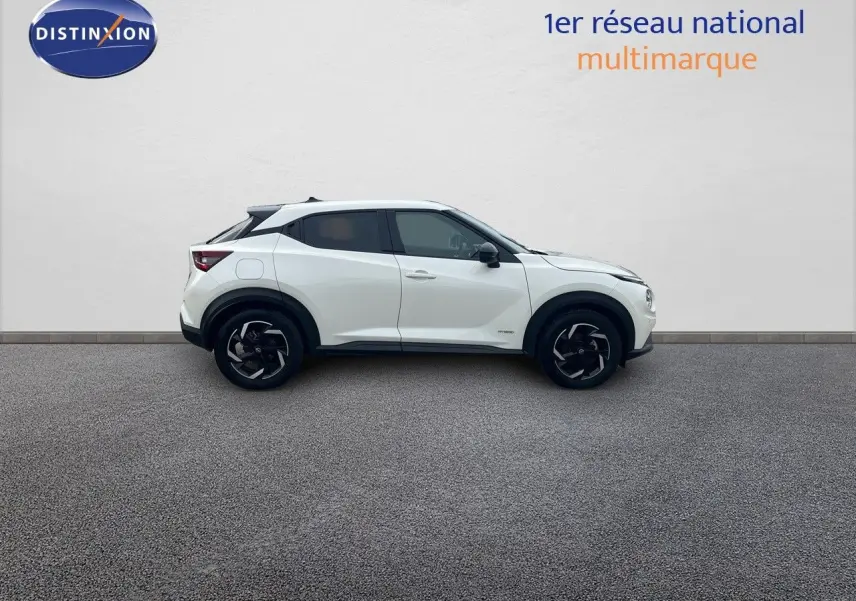 Vue de profil côté gauche d'un Nissan Juke blanc nacré 2024 avec jantes noires et toit contrasté noir.