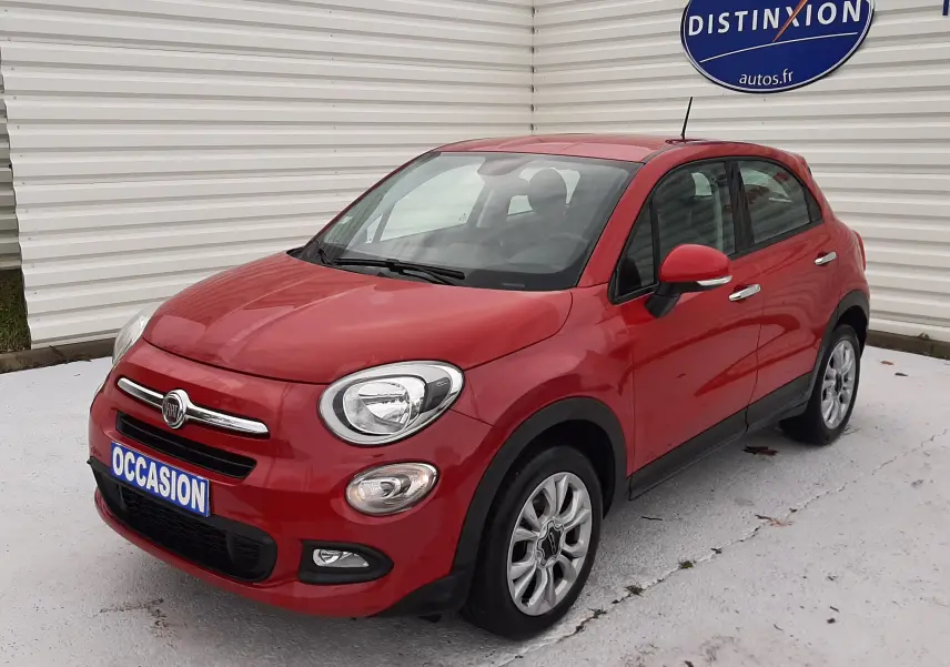 Fiat 500X rouge vue 3/4 avant droit, compacte avec jantes alliage et calandre chromée, stationnée devant un mur blanc.