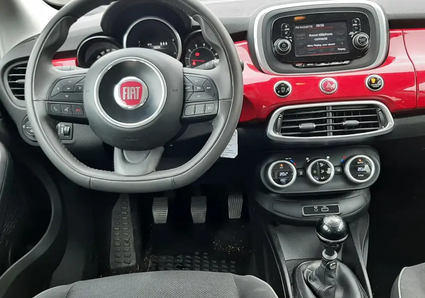 Vue intérieure avant de la Fiat 500X rouge de 2016, avec volant multifonction, tableau de bord rouge brillant et boîte manuelle.