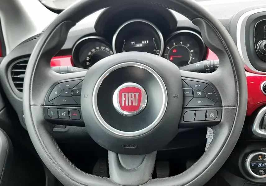 Vue rapprochée du volant noir avec logo rouge FIAT du tableau de bord d'une 500X rouge de 2016.