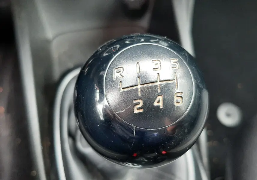 Gros plan sur le pommeau de la boîte manuelle 6 vitesses d'une Fiat 500X rouge, montrant les chiffres et la marche arrière.