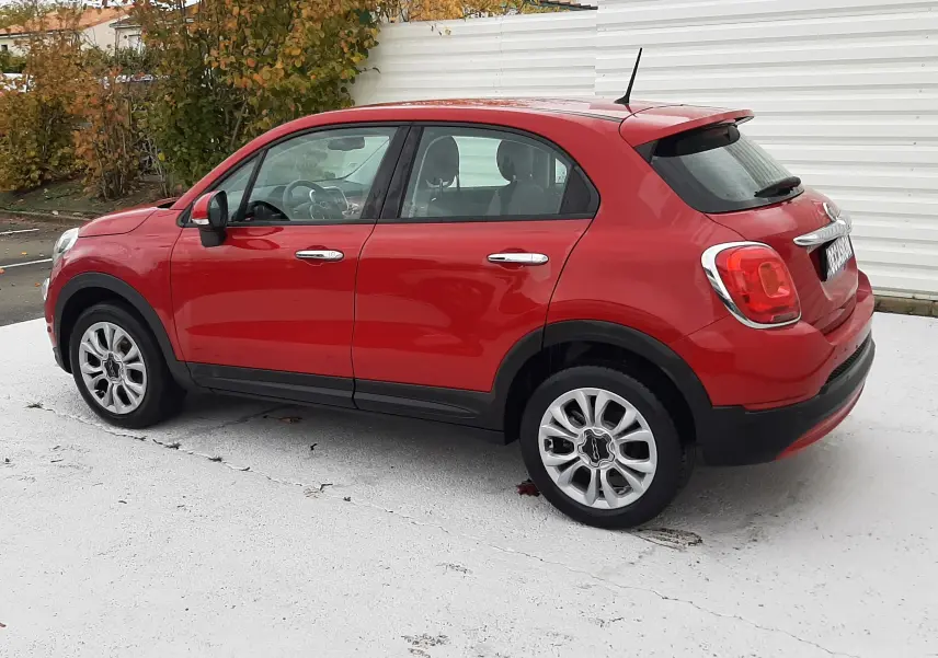Vue de profil côté droit d'un FIAT 500X rouge 2016 avec jantes alliage et poignées chromées.