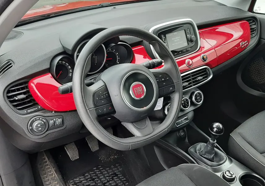 Intérieur de la Fiat 500X rouge vue côté conducteur, tableau de bord brillant rouge et volant multifonction noir.