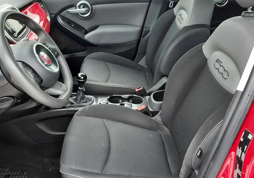 Vue intérieure côté conducteur d'une FIAT 500X rouge, sièges gris avec logo 500 brodé et tableau de bord assorti rouge.