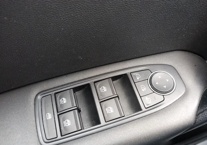 Gros plan sur les commandes des vitres et rétroviseurs côté conducteur d’un Renault Captur noir, intérieur tissu noir.