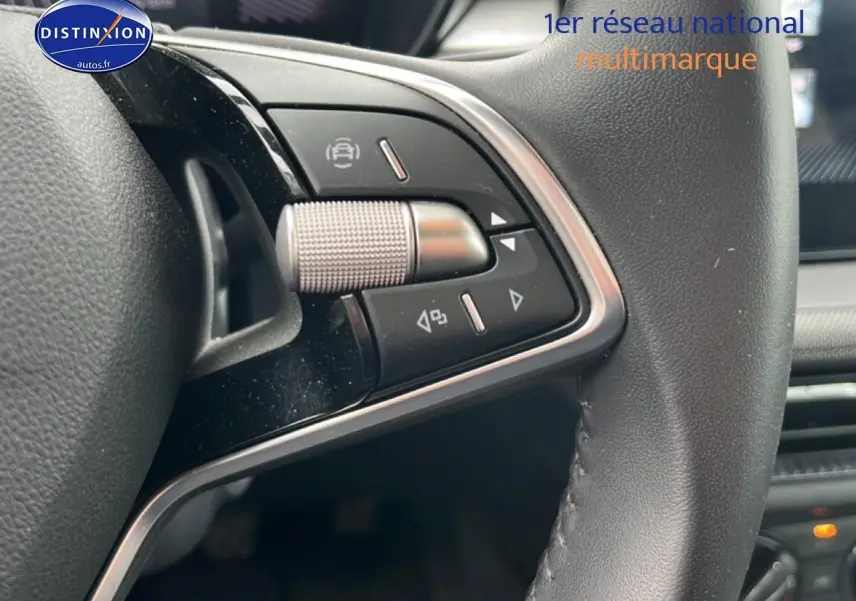 Gros plan sur les commandes gauche du volant cuir noir de la Skoda Fabia blanche, avec détails chromés et boutons multifonctions.