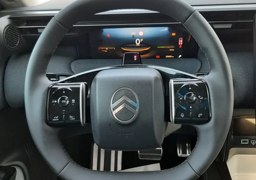 Vue rapprochée du volant noir de la Citroën C5 Aircross hybride 2026 avec tableau de bord numérique en arrière-plan.