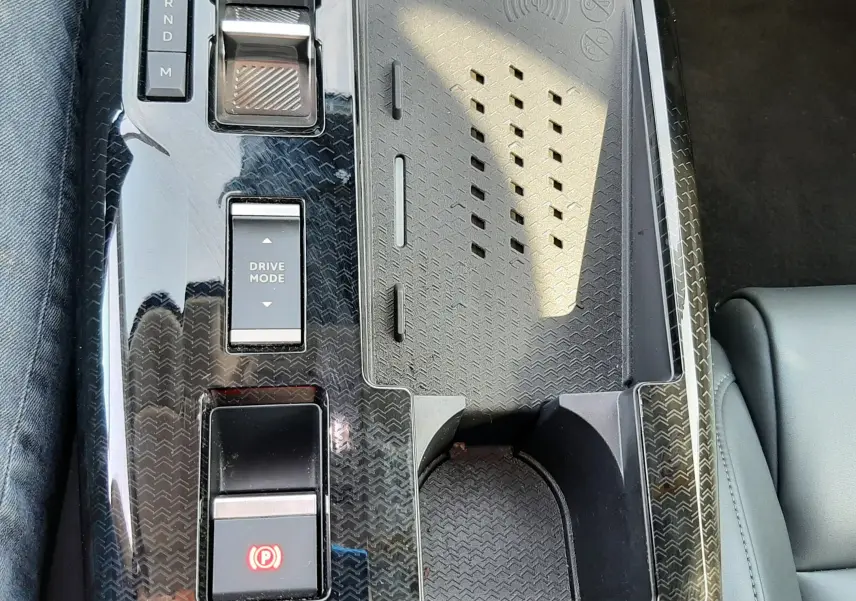 Vue rapprochée de la console centrale noire brillante du Citroën C5 Aircross hybride 2026 avec commandes de boîte auto et porte-gobelet.