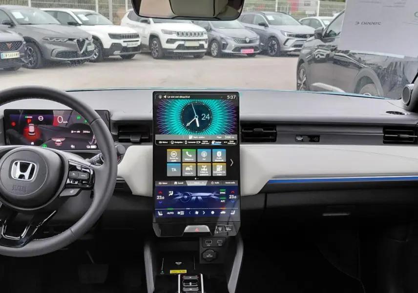 Vue intérieure avant du tableau de bord du Honda e:Ny1 bleu 2025 avec écran tactile vertical et éclairage d'ambiance bleu.
