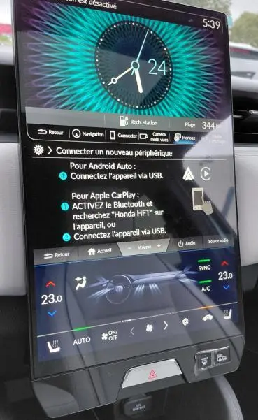 Vue rapprochée de l’écran tactile central du Honda e:Ny1 204 ch Advance 2025, affichant l’horloge et les réglages climatiques.