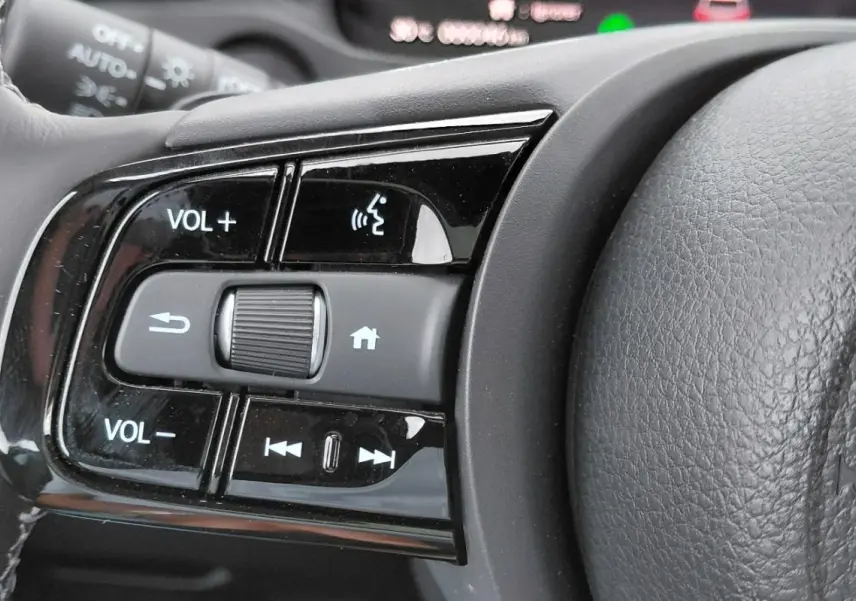 Gros plan sur les commandes de volume et multimédia au volant du Honda e:Ny1 204 ch Advance 2025, intérieur noir.