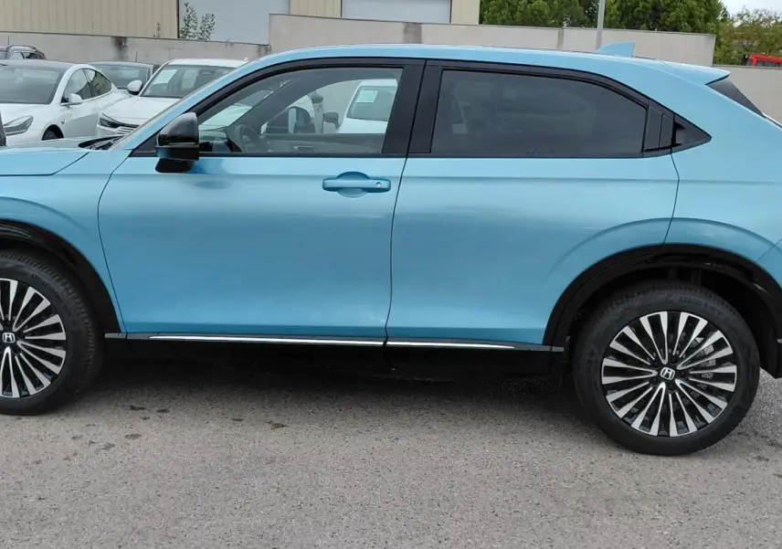 Vue de profil côté gauche d'un Honda e:Ny1 Advance 204 ch bleu électrique avec jantes stylisées en concession.