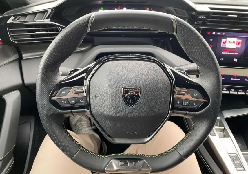 Vue rapprochée du volant GT noir avec surpiqûres vertes du Peugeot 308 Rouge Elixir, tableau de bord et écran tactile visibles.