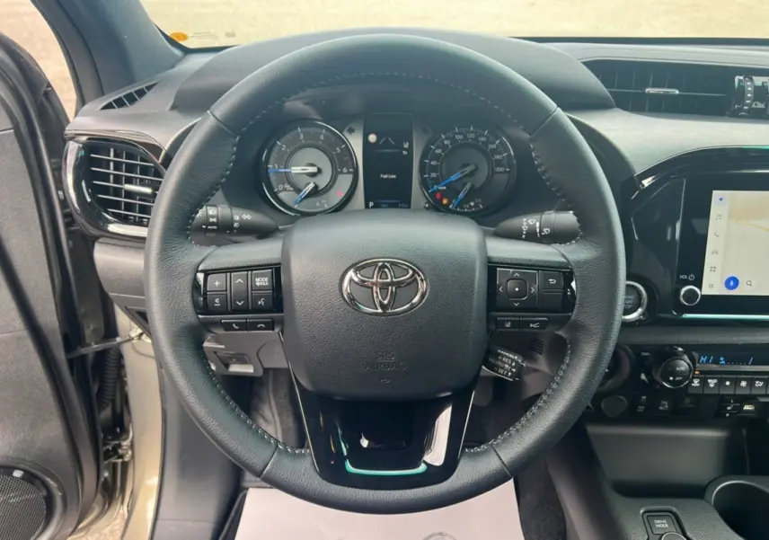 Vue intérieure centrée sur le volant du Toyota Hilux 2025, avec tableau de bord et écran tactile visibles.
