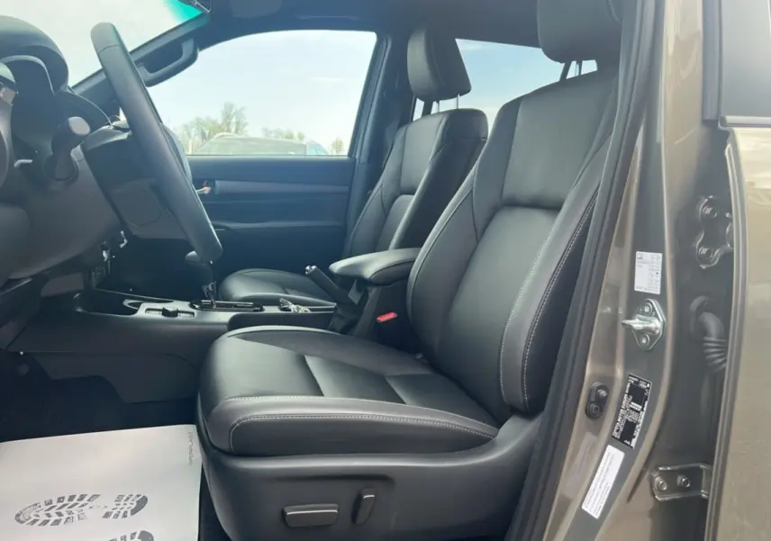 Vue intérieure côté conducteur du Toyota Hilux 2025 en bronze impérial, sièges en cuir noir et console centrale visible.