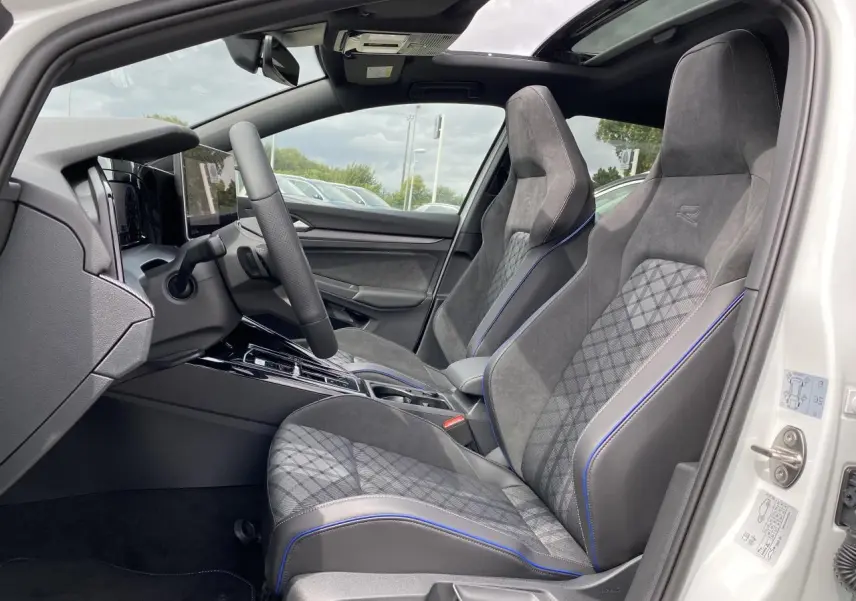 Intérieur côté conducteur d'une Volkswagen Golf 1.5 eTSI R-Line blanche, sièges sport gris avec surpiqûres bleues et toit panoramique.