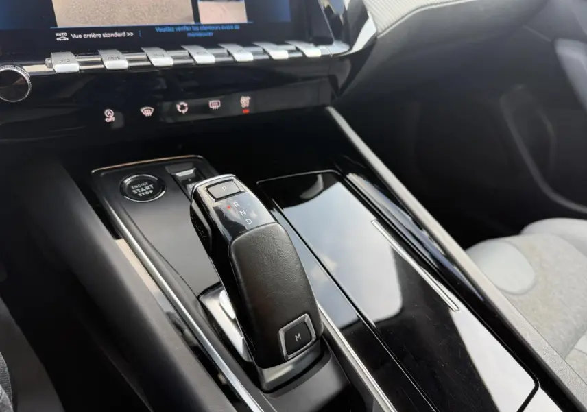 Gros plan sur la console centrale noire brillante de la Peugeot 508 bleu, avec levier de boîte automatique et bouton start/stop.