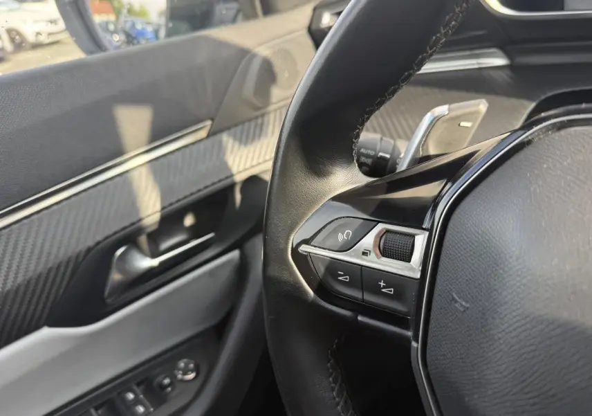 Détail du volant et de la porte côté conducteur avec décor carbone et commandes intégrées sur Peugeot 508 bleu.