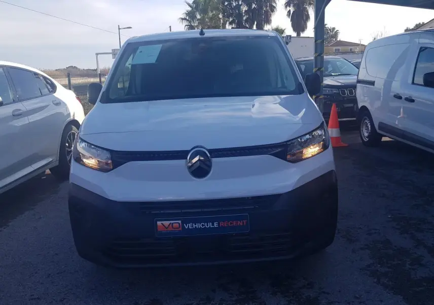 Vue avant d’un Citroën Berlingo blanc 2025 avec feux allumés, garé parmi d’autres véhicules en extérieur.