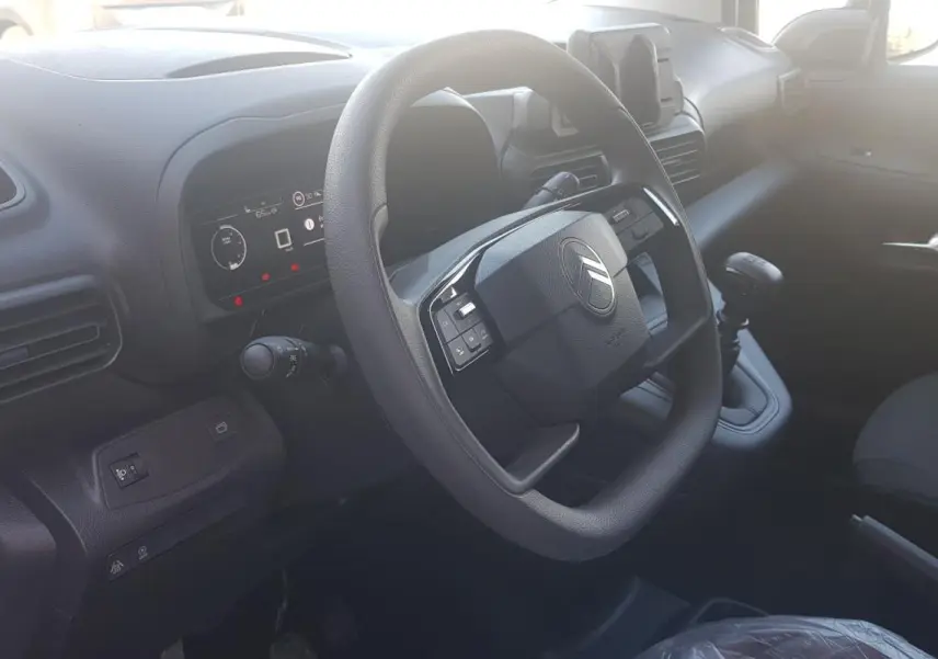 Vue intérieure du poste de conduite du Citroën Berlingo blanc, avec volant multifonctions et levier de vitesses manuel.