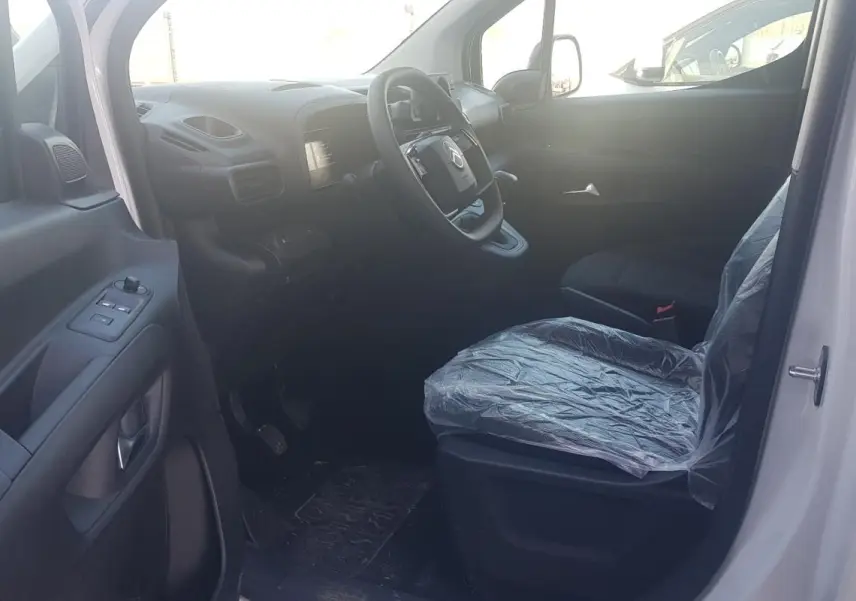 Vue intérieure côté conducteur du Citroën Berlingo blanc 2025, siège protégé par housse plastique et volant multifonctions.