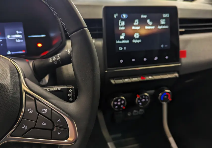 Vue intérieure rapprochée du tableau de bord et volant noir de la Renault Clio V avec écran tactile et commandes au volant.