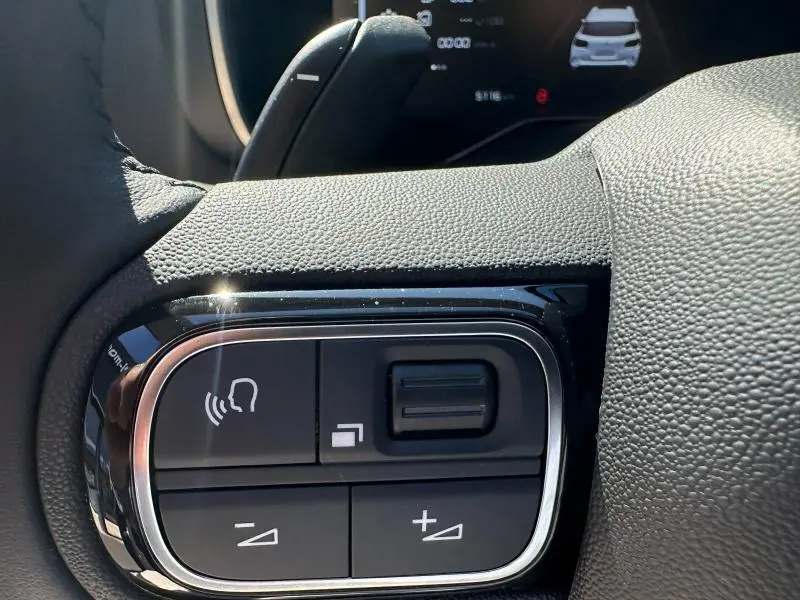 Gros plan sur les commandes de volume au volant du Citroën C5 Aircross 2025 en Noir Perla Nera, avec affichage numérique en arrière-plan.