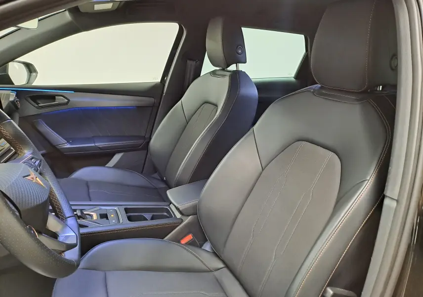 Vue intérieure côté conducteur de la CUPRA LEON ST 1.5 eTSI 150 DSG7 avec sièges noirs et surpiqûres cuivrées.