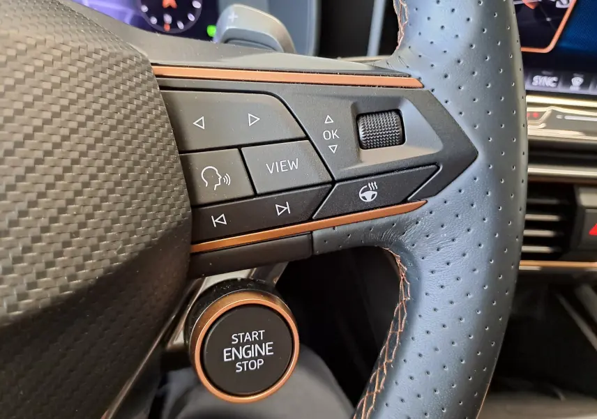 Gros plan sur la partie gauche du volant perforé noir avec surpiqûres cuivrées et bouton Start Engine Stop du CUPRA Leon ST 2025.
