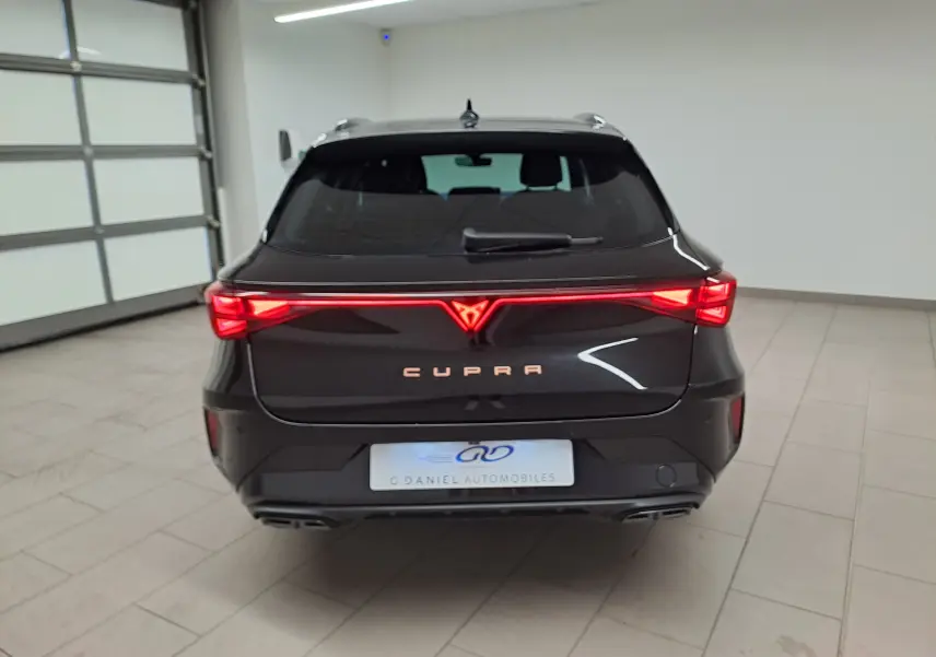 Vue arrière d'une CUPRA Leon ST 1.5 eTSI 150 DSG7 noire Minuit avec feux LED allumés en intérieur.