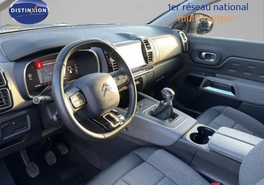 Vue intérieure côté conducteur du Citroën C5 Aircross gris, montrant le volant, tableau de bord numérique et levier de vitesse manuel.