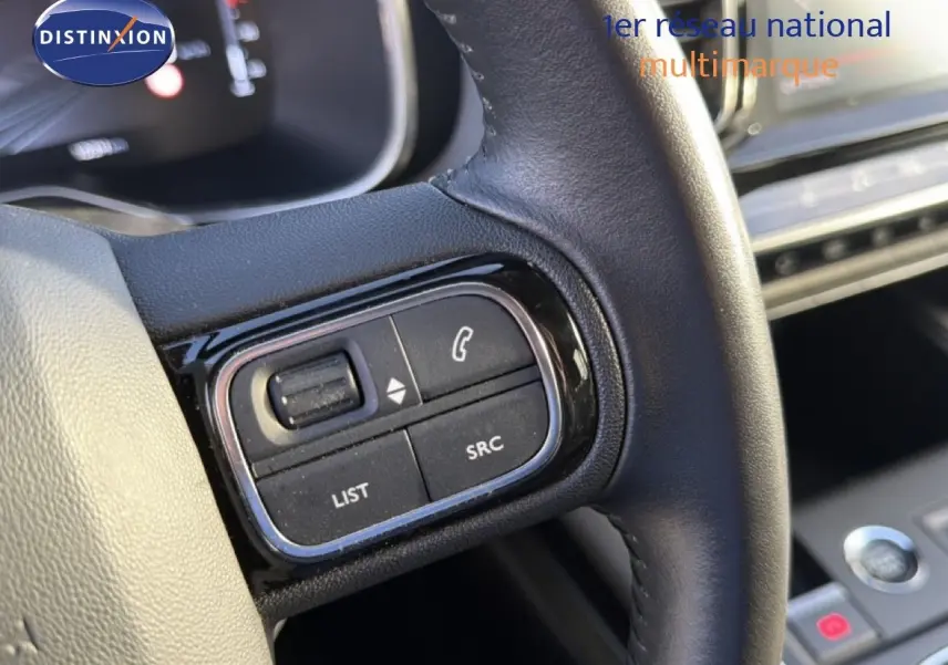 Gros plan sur les commandes gauche du volant en cuir noir du Citroën C5 Aircross gris Artense, tableau de bord en arrière-plan.