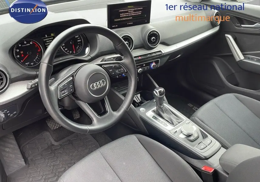 Vue intérieure côté conducteur de l'Audi Q2 35 TFSI 150CH S-Line 2023, volant multifonction et console centrale noire.