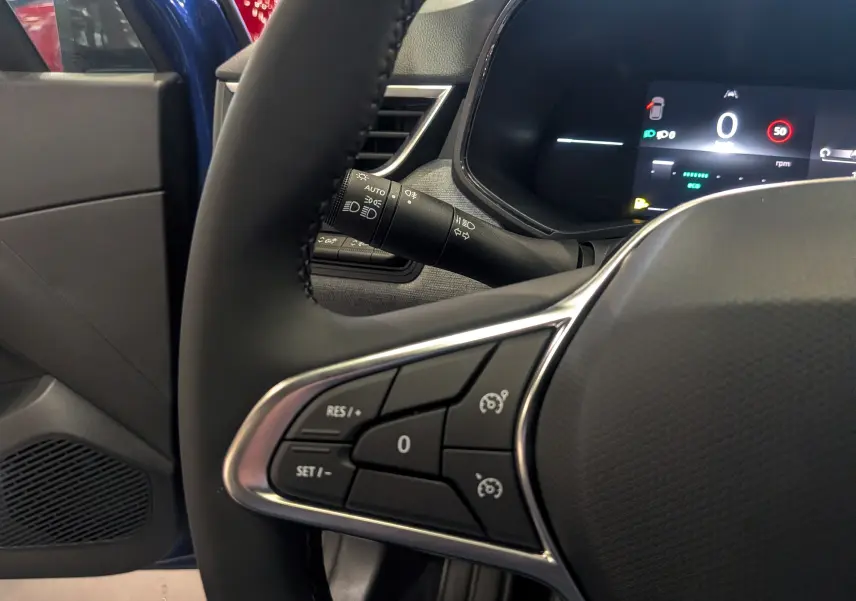 Vue rapprochée du volant et du tableau de bord numérique d'une Renault Clio V Bleu Iron, avec portière ouverte côté gauche.