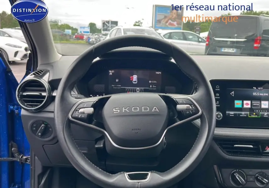 Vue intérieure centrée sur le volant cuir SKODA d'une Fabia bleue avec écran tactile et commandes au volant visibles.
