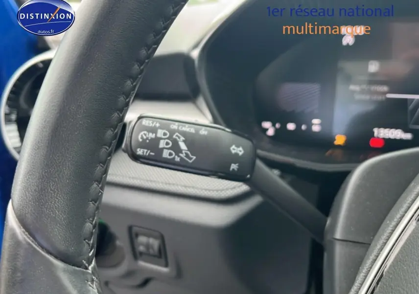 Gros plan sur le volant cuir noir et la commande de clignotant d'une Skoda Fabia bleue, tableau de bord numérique en arrière-plan flou.