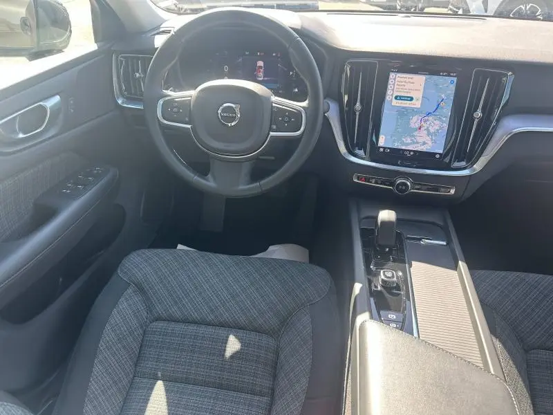 Vue intérieure avant du Volvo S60 B4 2024, volant multifonction, écran tactile central avec navigation, sièges tissu gris.