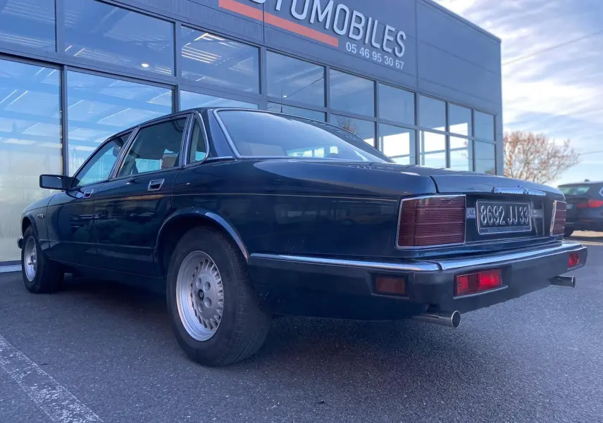 Jaguar XJ6 3.6 Sovereign bleu vue 3/4 arrière droit, avec feux arrière rectangulaires et double sortie d'échappement.