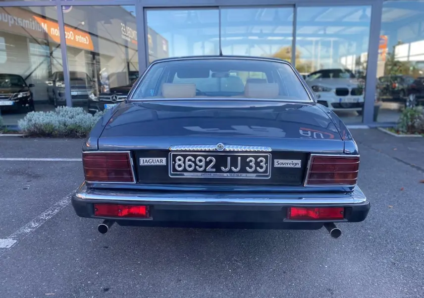Vue arrière d'une Jaguar XJ6 3.6 Sovereign bleu de 1987 avec plaques et feux rouges rectangulaires visibles.