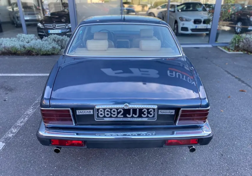 Vue arrière d'une Jaguar XJ6 3.6 Sovereign bleue de 1987 avec plaques noires et feux rectangulaires rouges.