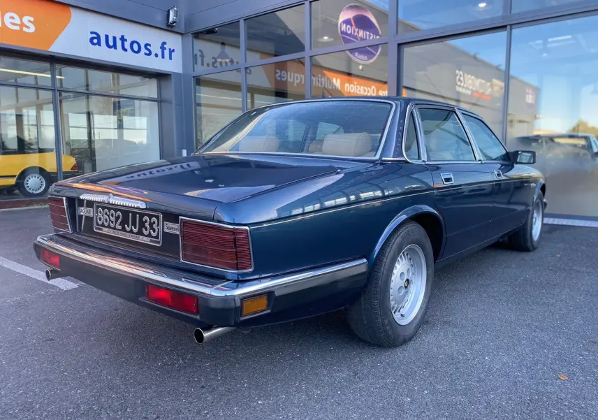 Vue 3/4 arrière droite d'une Jaguar XJ6 3.6 Sovereign bleu foncé de 1987 avec plaques françaises et jantes alliage.