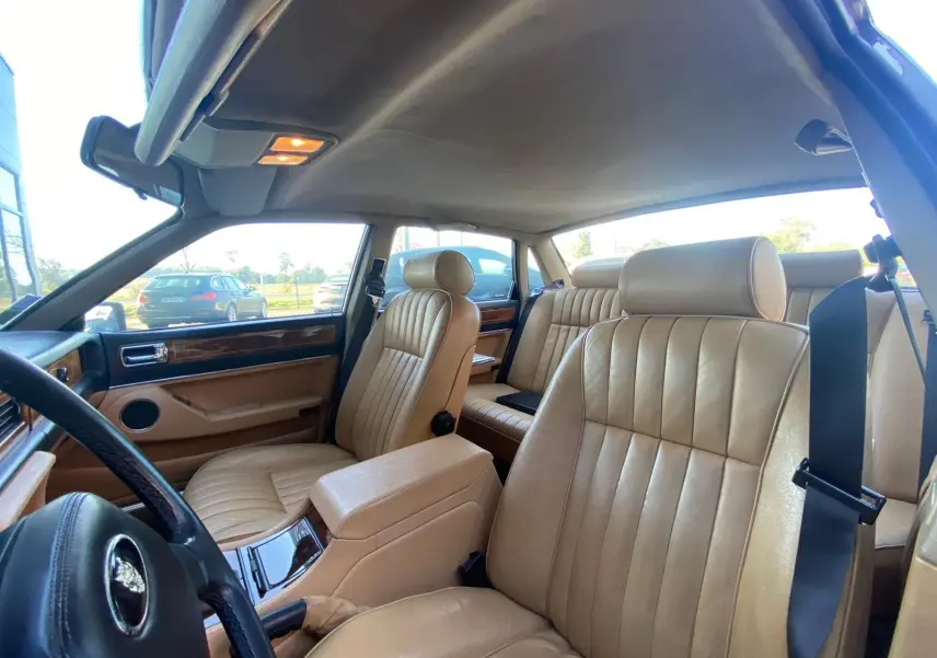 Intérieur beige cuir de la Jaguar XJ6 3.6 Sovereign 1987, vue côté conducteur avec planche de bord en bois.